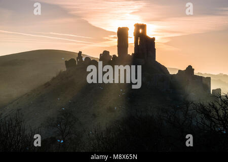 Corfe Castle, Dorset, Großbritannien. 21. März 2018. UK Wetter. Sonnenstrahlen durchscheinen und um die Silhouette der Ruinen von Corfe Castle in Dorset an einem klaren hellen Morgen kurz nach Sonnenaufgang. Foto: Graham Jagd-/Alamy Leben Nachrichten. Stockfoto