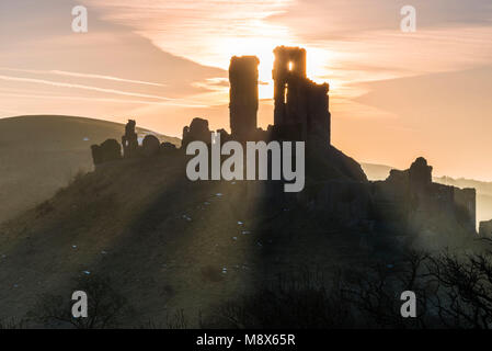 Corfe Castle, Dorset, Großbritannien. 21. März 2018. UK Wetter. Sonnenstrahlen durchscheinen und um die Silhouette der Ruinen von Corfe Castle in Dorset an einem klaren hellen Morgen kurz nach Sonnenaufgang. Foto: Graham Jagd-/Alamy Leben Nachrichten. Stockfoto