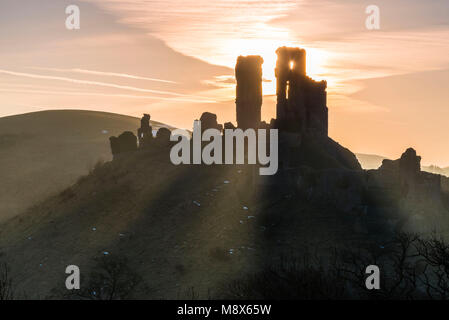 Corfe Castle, Dorset, Großbritannien. 21. März 2018. UK Wetter. Sonnenstrahlen durchscheinen und um die Silhouette der Ruinen von Corfe Castle in Dorset an einem klaren hellen Morgen kurz nach Sonnenaufgang. Foto: Graham Jagd-/Alamy Leben Nachrichten. Stockfoto