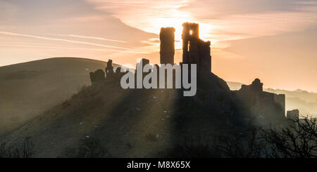 Corfe Castle, Dorset, Großbritannien. 21. März 2018. UK Wetter. Sonnenstrahlen durchscheinen und um die Silhouette der Ruinen von Corfe Castle in Dorset an einem klaren hellen Morgen kurz nach Sonnenaufgang. Foto: Graham Jagd-/Alamy Leben Nachrichten. Stockfoto