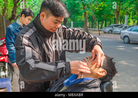 Barber Rasur Mann Straße, ein Barbier am Straßenrand rasiert einen Kunden in der Nähe von West Lake in Hanoi, Vietnam.