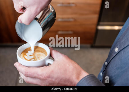 Professionelle barista Gießen gedämpfte Milch aus Edelstahl Becher in die Tasse Kaffee, latte Art auf Cappuccino Stockfoto