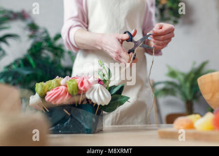 Bild von Floristen mit Scheren - Schneiden von Seilen am Tisch mit Blumenstrauß, Marmelade, Eibisch im Zimmer Stockfoto