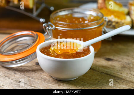 Frühstück mit hausgemachten Bio Marmelade in einer kleinen weißen Schale mit größeren Betrag in einem Einmachglas auf einer alten Küche aus Holz Tisch c Stockfoto