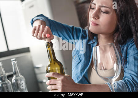 Junge weibliche alkoholische soziale Probleme am Tisch Öffnen der Flasche Wein in der Nähe sitzen - bis sucht Stockfoto