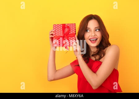 Junge Frau studio isoliert auf gelbe Wand das Tragen der roten Kleid schütteln vorhanden, neugierig lächelnd heiter Stockfoto