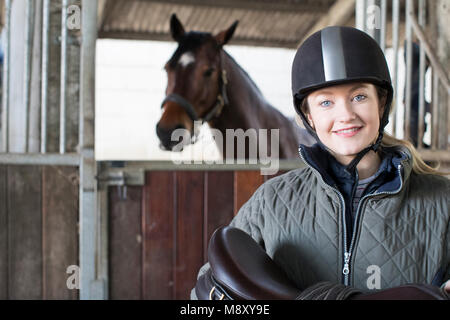 Portrait von weiblichen Besitzer Holding Sattel in stabilen mit Pferd Stockfoto
