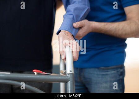 Der ältere Mann die Hände auf Gehhilfe mit Sorgfalt Arbeiter im Hintergrund Stockfoto