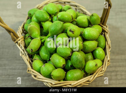 Korb voller grüner Junge Walnüsse in Schalen auf hölzernen Tisch Stockfoto