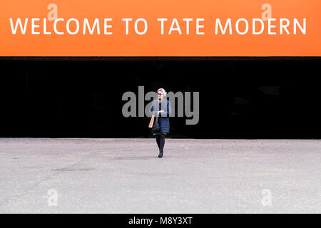 Eine reife Frau vor ein willkommenes Zeichen über einen Eingang zu Tate Modern auf der South Bank in London. Stockfoto