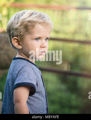 Wundervolle baby boy, blaue Augen und blondes Haar schaut in die Leere in den Garten, natürliches Licht. Stockfoto