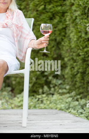 Einer Frau mit einem Glas Rose Wein auf einer Terrasse im Freien mit grünem Hintergrund Stockfoto