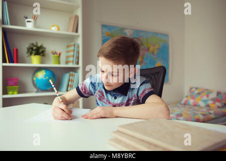 Wenig smart School Junge die Hausaufgaben am Schreibtisch in seinem Zimmer Stockfoto