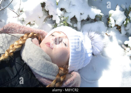 Eine junge Frau mit warmer Kleidung und geschlossenen Augen liegt im Schnee. Ein Tagtraum Szene. Stockfoto