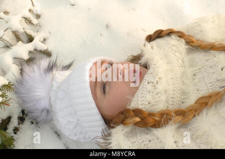 Eine junge Frau mit warmer Kleidung liegt im Schnee. Ein Tagtraum Szene. Stockfoto