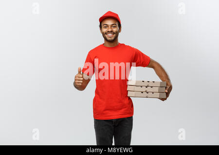 Lieferung Konzept - Portrait von Happy African American delivery man Holding Box Pakete und zeigt Thumps up. Auf Grau studio Hintergrund isoliert. Kopieren Sie Platz. Stockfoto