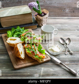 Croissants mit geräuchertem Lachs, Quark, frische Salate und Kräuter auf einer hölzernen Hintergrund. Stockfoto