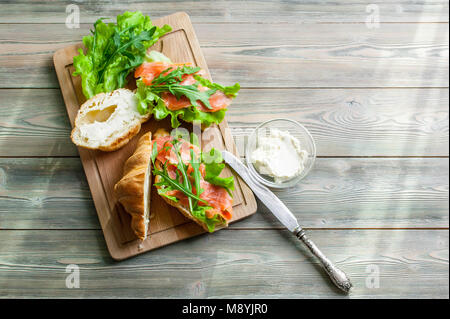 Croissants mit geräuchertem Lachs, Quark, frische Salate und Kräuter auf einer hölzernen Hintergrund. Stockfoto