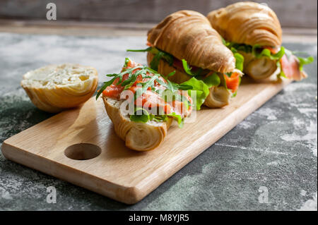 Croissants mit geräuchertem Lachs, Quark, frische Salate und Kräuter auf einer hölzernen Hintergrund. Stockfoto