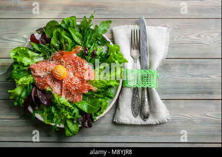 Salat mit geräuchertem Lachs, Eigelb, frischen Salat, Rucola, Spinat und Zuckerrüben Sprossen in eine Platte auf einem hölzernen Hintergrund. Ansicht von oben Stockfoto