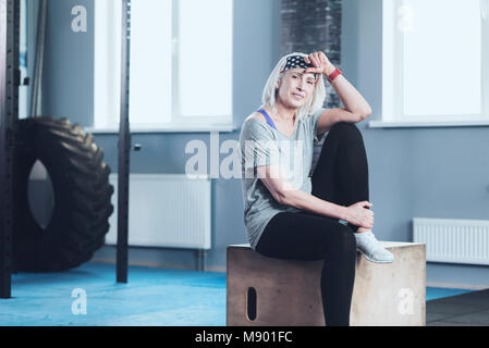 Hübsche reife Frau lächelnd, während im Fitnessstudio ruhen Stockfoto
