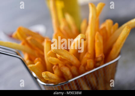 Nahaufnahme der einige leckere Pommes frites in einem Metallkorb auf einem grauen rustikalen Holztisch serviert. Stockfoto