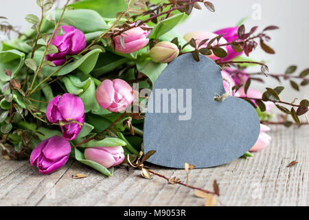 Schönen Blumenstrauß rosa und violett Tulpen mit einem Herzen aus Holz Hintergrund Stockfoto