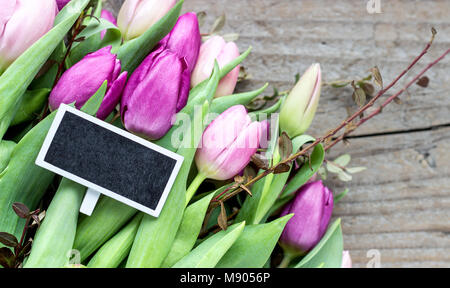 Blick von oben auf ein Bouquet von rosa und violett Tulpen mit einem Schwarzen Brett auf einem hölzernen Hintergrund Stockfoto