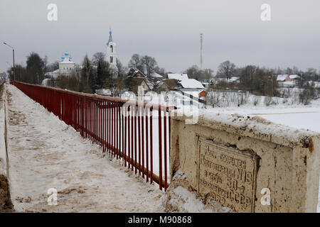 Blick auf ein Dorf mit Kirche durch Schnee und eine Brücke über einen kleinen Fluss gebaut 50. Jahrestag der UDSSR, Porechye Dorf zu gedenken, Ner Stockfoto