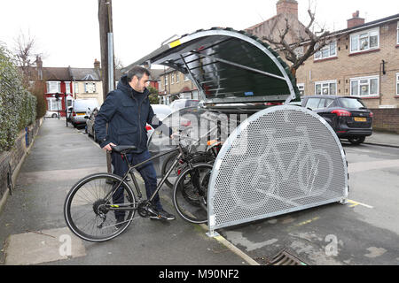 Ein Radfahrer Orte sein Fahrrad in eine sichere auf der Straße Fahrrad geschäft kürzlich auf einer ruhigen Londoner Straße installiert. Stockfoto