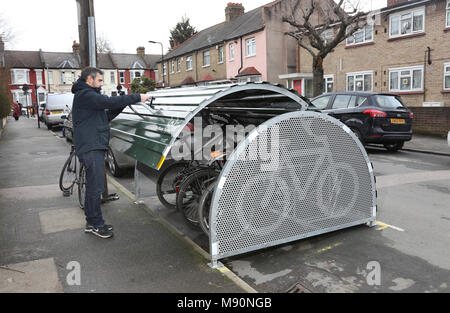 Ein Radfahrer Orte sein Fahrrad in eine sichere auf der Straße Fahrrad geschäft kürzlich auf einer ruhigen Londoner Straße installiert. Stockfoto