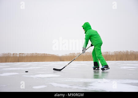 Eishockeyspieler in der Grünen insgesamt auf der großen natürlichen Eis des zugefrorenen Neusiedler See trotzen Stumpf trüb und kalten Winter. Stockfoto