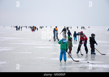 Vater und Kinder spielen unter anderem Eishockey Eislaufen auf den zugefrorenen Neusiedler See in Stumpf trübe Winterwetter. Stockfoto