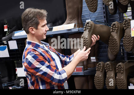 Mann wählt Gummistiefel für Jagd und Fischerei in einem Geschäft Stockfoto