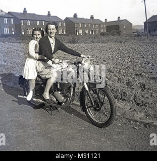 1950, historische, außerhalb einige ländliche Häuschen, von einem gepflügten Feldes, eine Mutter und Tochter zusammen sitzen auf dem Motorrad ist ihr Vati, England, UK. Stockfoto