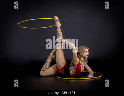 Die Contortionistin Frau im Bühnenkostüm mit Reifen. Studio auf dunklem Hintergrund aufgenommen. Stockfoto