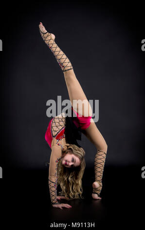 Die Contortionistin Frau im Bühnenkostüm mit Reifen. Studio auf dunklem Hintergrund aufgenommen. Stockfoto