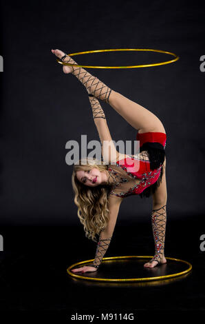 Die Contortionistin Frau im Bühnenkostüm mit Reifen. Studio auf dunklem Hintergrund aufgenommen. Stockfoto