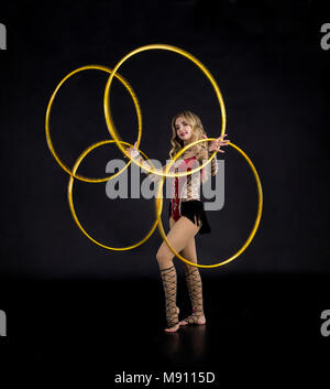 Die Contortionistin Frau im Bühnenkostüm mit Reifen. Studio auf dunklem Hintergrund aufgenommen. Stockfoto