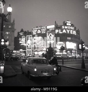 1960, historische Bild von London Piccadilly Circus am Abend mit Fahrzeugen und dem berühmten Neonröhren und Werbetafeln für Marken wie "Spieler Zigaretten' und 'Coca-cola'. Stockfoto