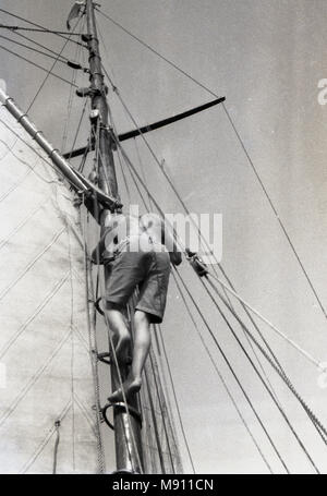 1970er Jahre, Sailor, Klettern oder aloft einem Mast auf einem Boot auf seinem eigenen unversorgten, England, UK. Stockfoto