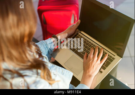 Frau seine Reise am Flughafen Terminal wartet, sitzt auf einem Stuhl und tippen auf dem Laptop suchen Seite. Von der Seite. Stockfoto