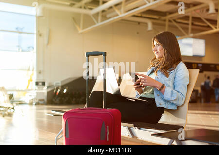 Flughafen jungen weiblichen Passagier auf Smartphone und Laptop im Terminal Hall beim Warten auf ihren Flug Stockfoto