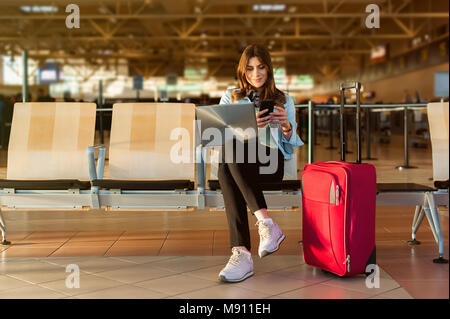 Flughafen jungen weiblichen Passagier auf Smartphone und Laptop im Terminal Hall beim Warten auf ihren Flug Stockfoto