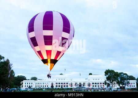 Ein farbenfroher violett-weißer Heißluftballon spritzt Feuer und heiße Luft in den Ballon, wenn er am Old Parliament House in Canberra vorbeikommt Stockfoto