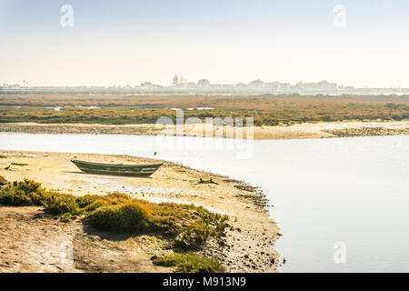 Grüne Boot bei Ebbe in der Ria Formosa mit Gebäuden von Faro Beach als Hintergrund, Portugal Stockfoto