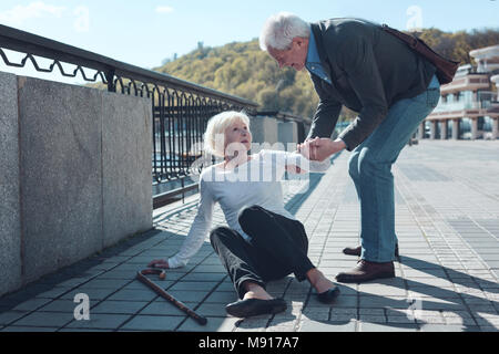 Eingedenk Mann helfen älteren weiblichen Fremder bis zu stehen Stockfoto