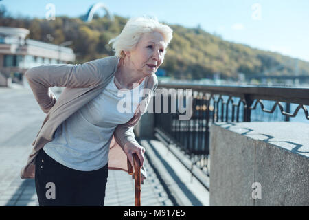 Ältere Dame hält ihre Hände auf dem Rücken, während die Gefühl Schmerz Stockfoto