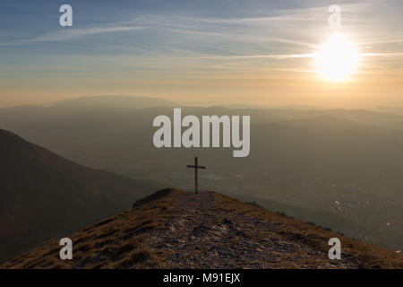 Kreuz auf dem Gipfel des Mt. Serrasanta (Umbrien, Italien), mit warmen goldenen Stunde Farben und die Sonne tief am Horizont Stockfoto