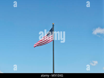 Eine amerikanische Flagge auf einem Black Metal Pole weben in den klaren Himmel am 4. Juli. Stars and Stripes auf einem Hintergrund ideal für Copyspace. Stockfoto